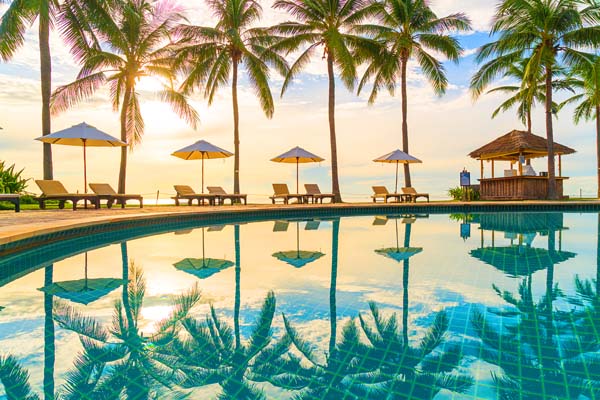 Beautiful luxury umbrella and chair around outdoor swimming pool in hotel and resort with coconut palm tree on sunset or sunrise sky - holiday and vacation concept