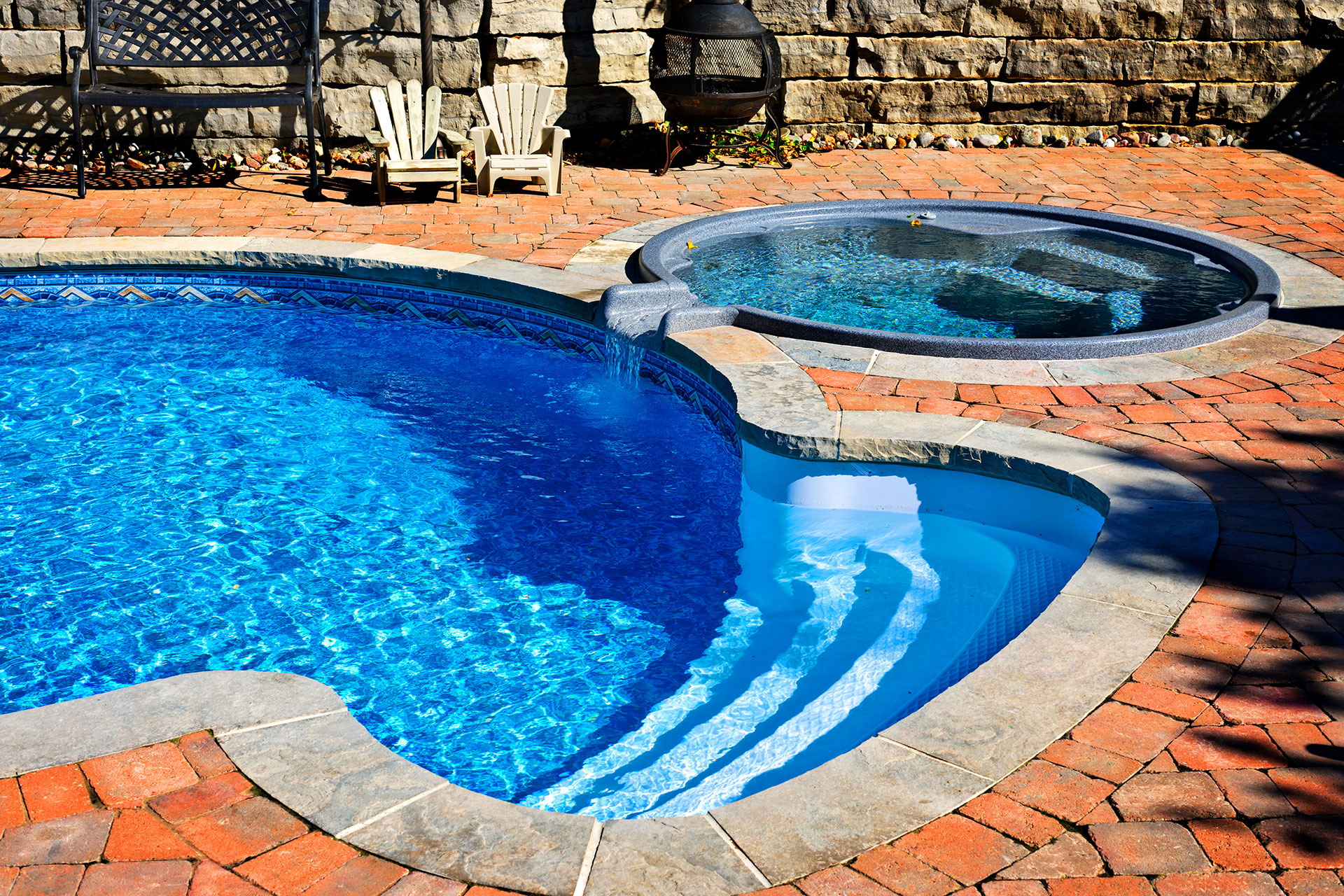 Freeform inground pool with attached spa and brick paver patio in residential backyard