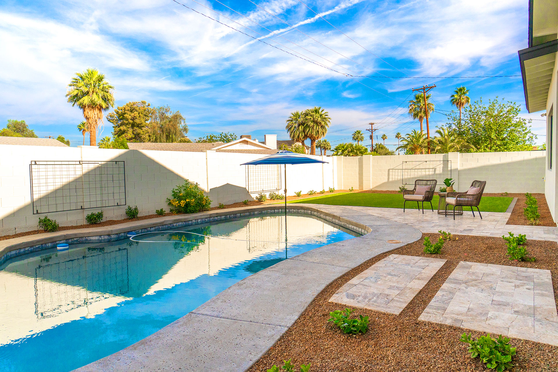 Rectangular backyard swimming pool with travertine deck and patio furniture under palm trees